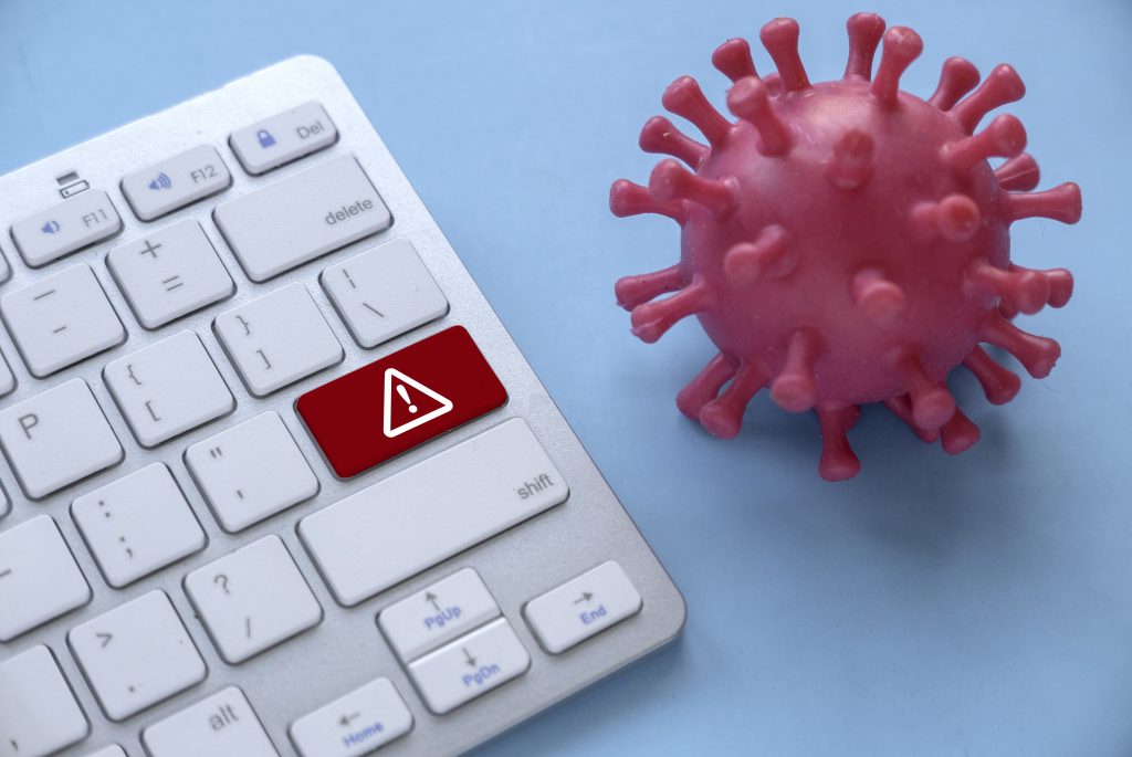 Keyboard with warning key and pink virus model, symbolizing computer security threats and malware risks.