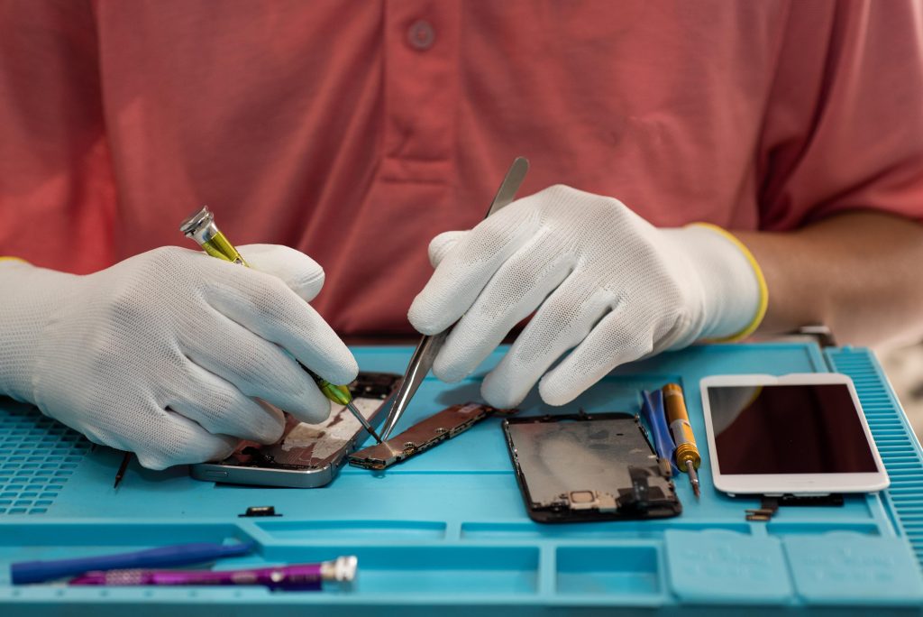 Technician repairing an iPhone with tools on a blue workbench, emphasizing expert iPhone repair services in Murray Bridge.