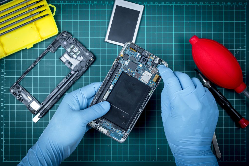 Technician in blue gloves repairing a smartphone, surrounded by tools and components on a green work surface, illustrating affordable phone repair services in Murray Bridge.