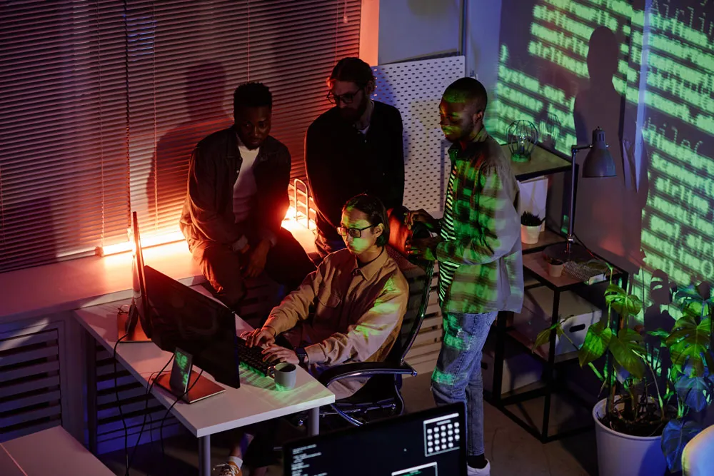 Group of individuals collaborating around a computer, with code projected on the wall, representing teamwork in addressing computer issues, relevant to virus cleaning services.