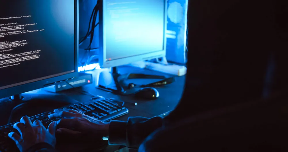 Person typing on a keyboard in front of multiple computer screens displaying code, illustrating hacking and computer security themes relevant to tech support services in South Broken Hill.