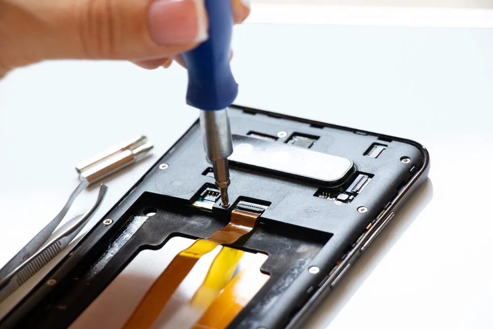Hand holding screwdriver repairing smartphone internals, showcasing phone repair services for issues like screen replacements and battery fixes.