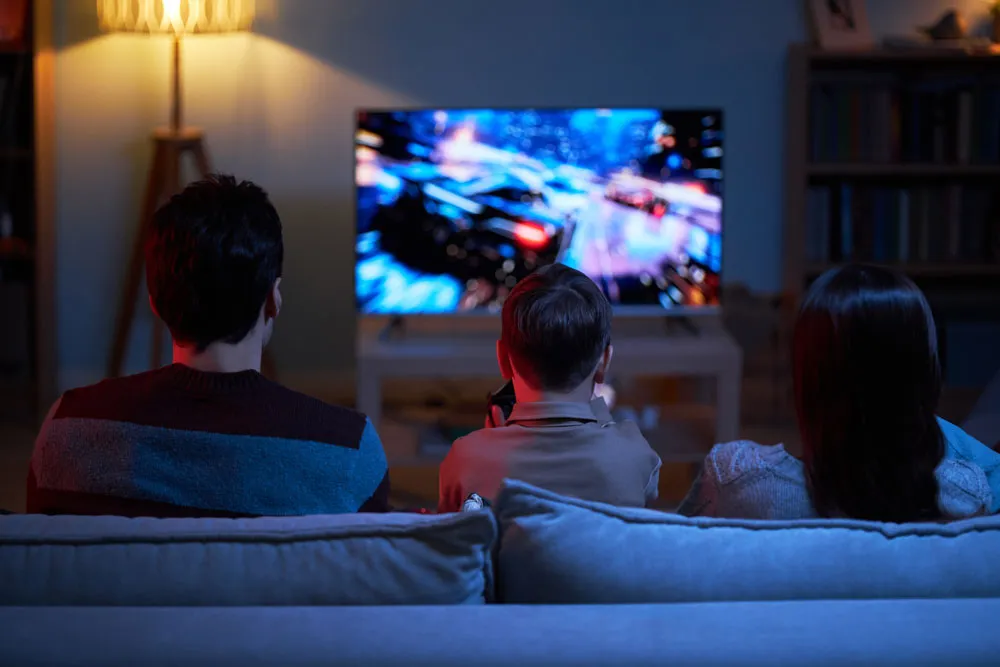 Family enjoying gaming together on a couch, focused on a vibrant gaming console display in a cozy living room setting.