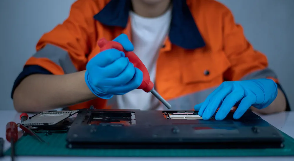 Technician in blue gloves repairing a laptop with a screwdriver, surrounded by tools, representing professional virus and malware removal services in Murray Bridge.