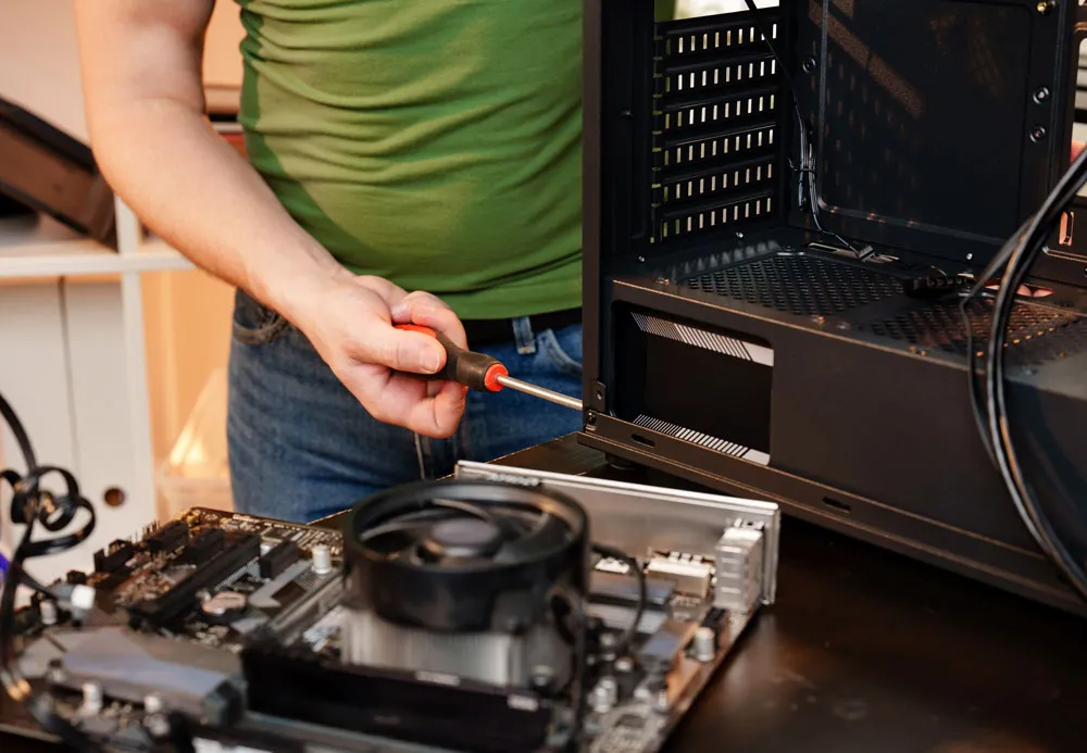 Person using a screwdriver to repair a computer, with a motherboard and cooling fan visible on a work surface, illustrating computer repair services offered by BizUp in Murray Bridge.