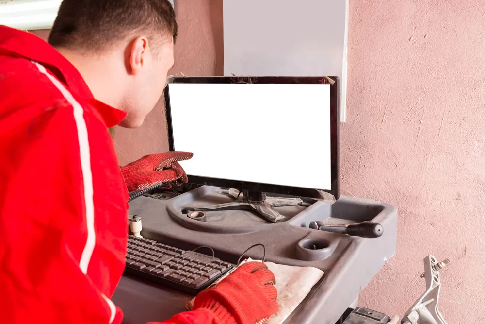 Technician in red overalls inspecting a computer monitor in a repair workspace, highlighting computer repair services offered by BizUp.
