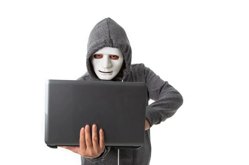 Person in a grey hoodie and white mask holding a laptop, representing cybersecurity threats and the need for malware removal services in Murray Bridge by Bizup.
