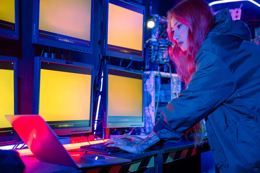 Person with long red hair working on a laptop in a tech environment with multiple computer monitors, illustrating computer repair services at Bizup in Murray Bridge.