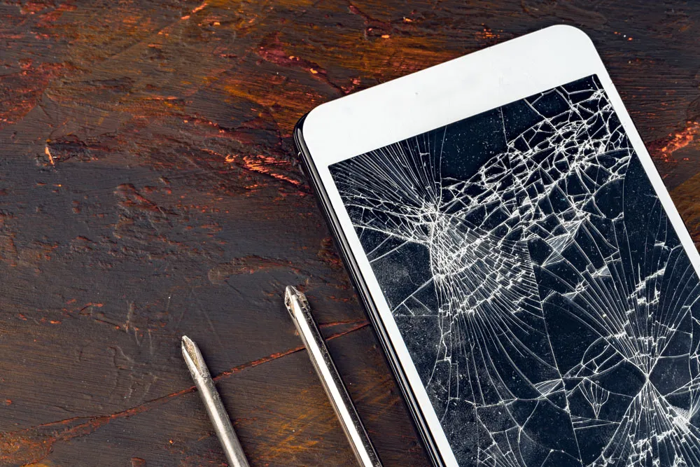 Broken smartphone screen on wooden surface with repair tools, illustrating expert iPhone repairs offered by Bizup in Murray Bridge.