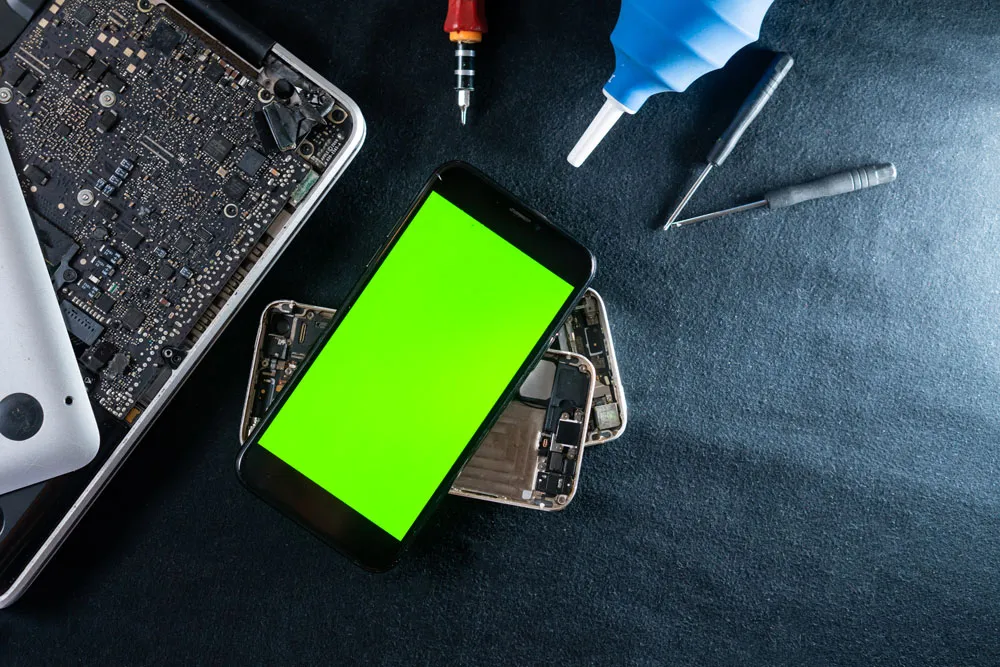 Smartphone with green screen placed on disassembled phone parts and repair tools, representing phone virus repair services in Murray Bridge.