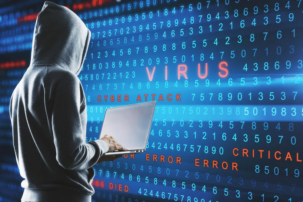 Hooded figure using laptop in front of digital backdrop displaying "VIRUS," "CYBER ATTACK," and error messages, illustrating malware threats and cybersecurity issues relevant to virus and malware removal services.