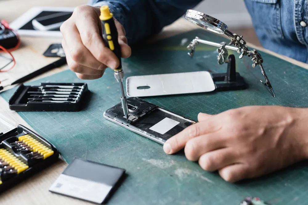 Technician repairing smartphone using screwdriver and tools on workbench, illustrating local phone repair services in Murray Bridge.