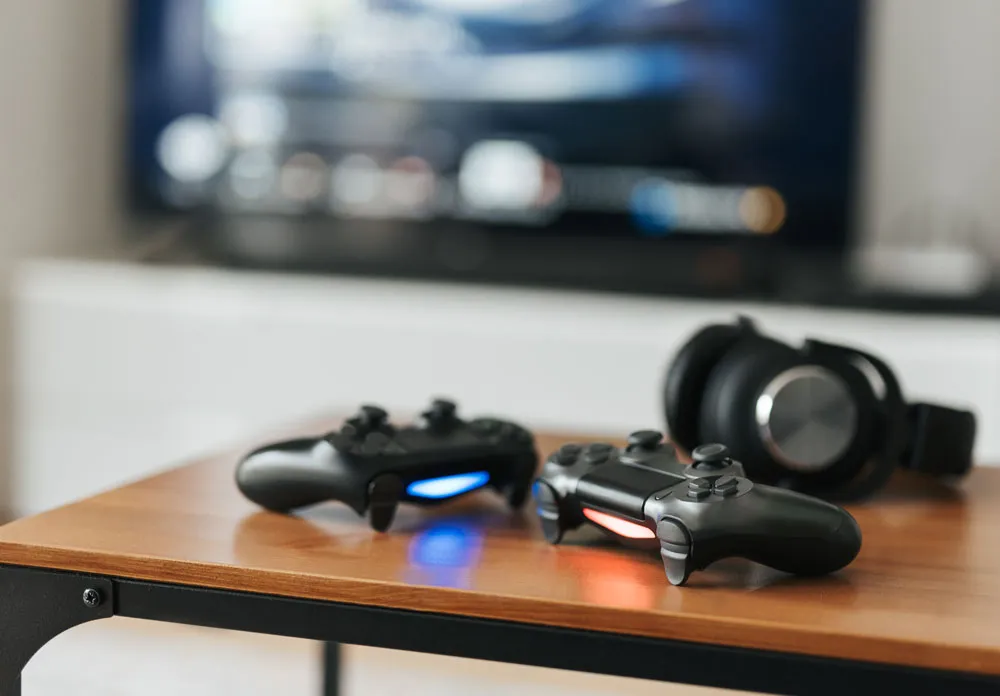 Gaming console controllers on a wooden table with headphones, set against a blurred television screen, representing gaming entertainment in Broken Hill.