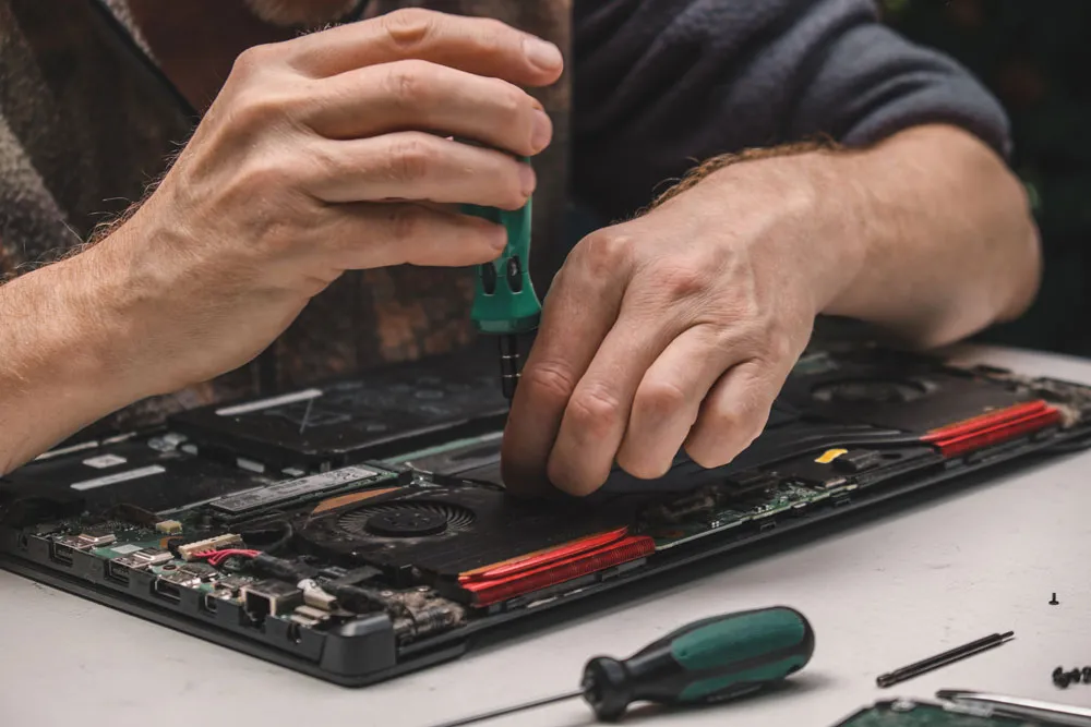 Hands repairing a laptop with a screwdriver, showcasing computer repair services relevant to affordable assistance in Murray Bridge.