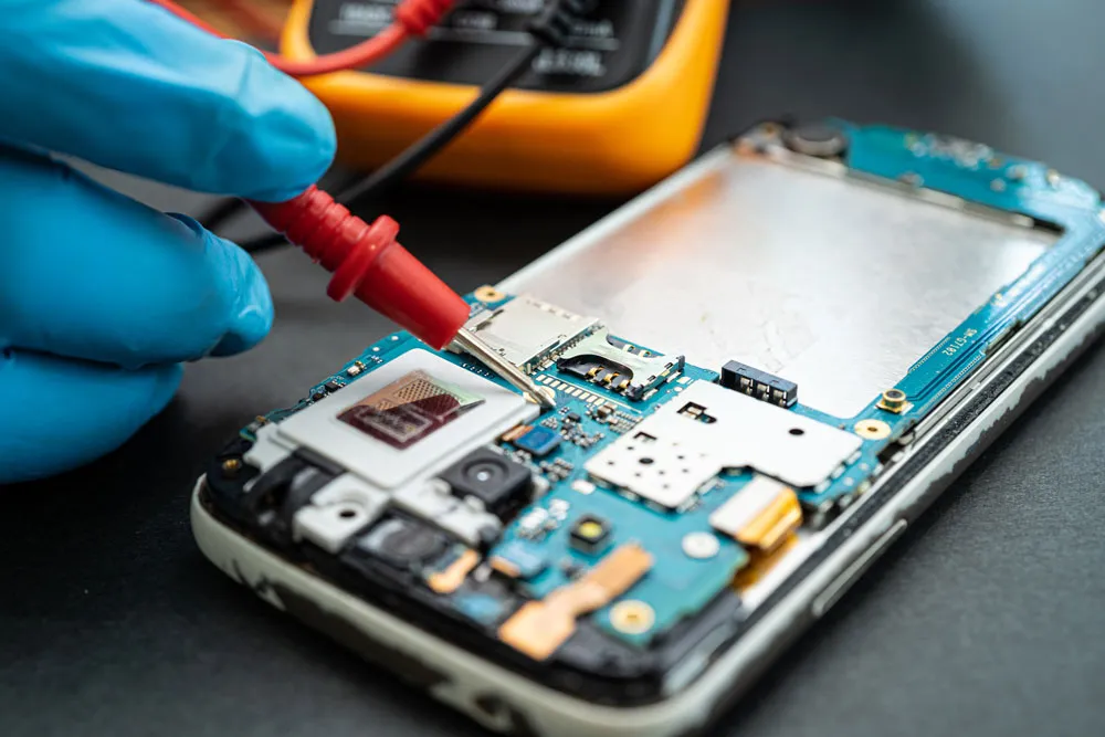Technician repairing smartphone circuit board with multimeter, highlighting phone virus repair services in Broken Hill.