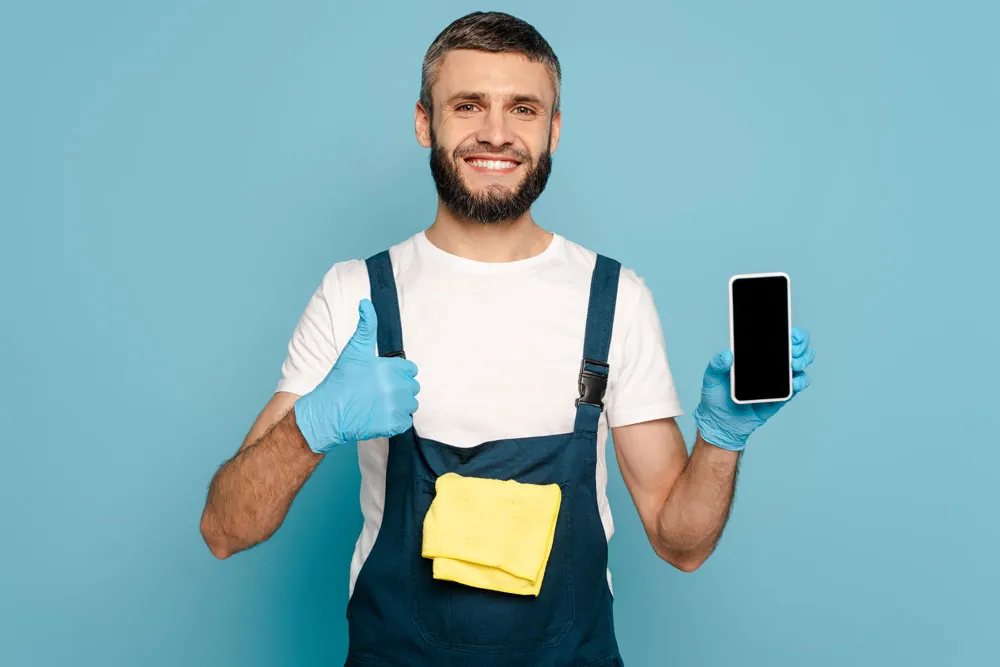 Man in blue overalls and gloves holding a smartphone and giving a thumbs up, representing phone virus repair services in Broken Hill.