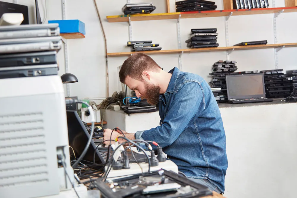 Technician repairing gaming consoles in a workshop, surrounded by tools and devices, illustrating local gaming console repair services in Murray Bridge.