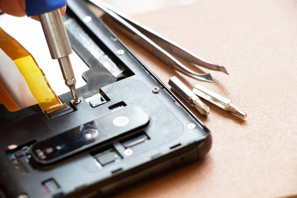 Close-up of smartphone repair with screwdriver tightening screws, surrounded by repair tools, illustrating quick and affordable phone repair services in Broken Hill.